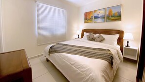 A neatly arranged bedroom with a bed, bedside lamps, a ceiling fan, and a window with blinds.