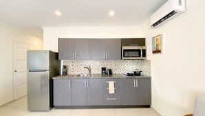 A compact kitchen with grey cabinets, a stainless steel refrigerator, a microwave, and a tiled backsplash.