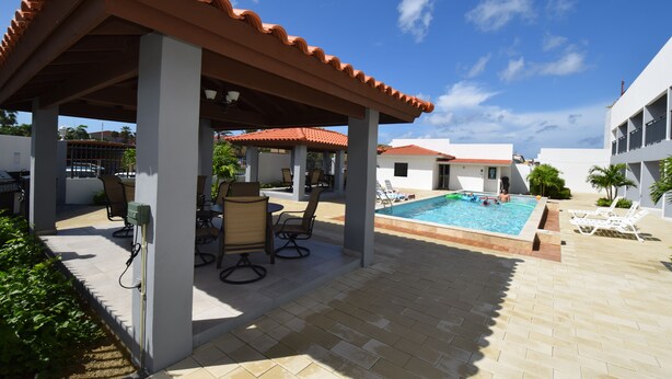 A covered outdoor area with a pool, lounge chairs, and a pergola.