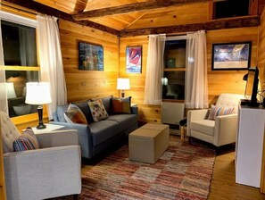 Relax in this inviting living room with a sofa set, armchair, and ottoman, surrounded by artwork and large windows.