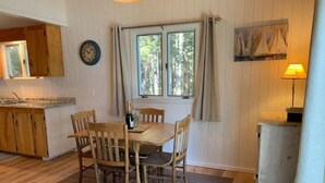 Un comedor con una mesa y sillas de madera, una ventana con cortinas y un reloj en la pared.