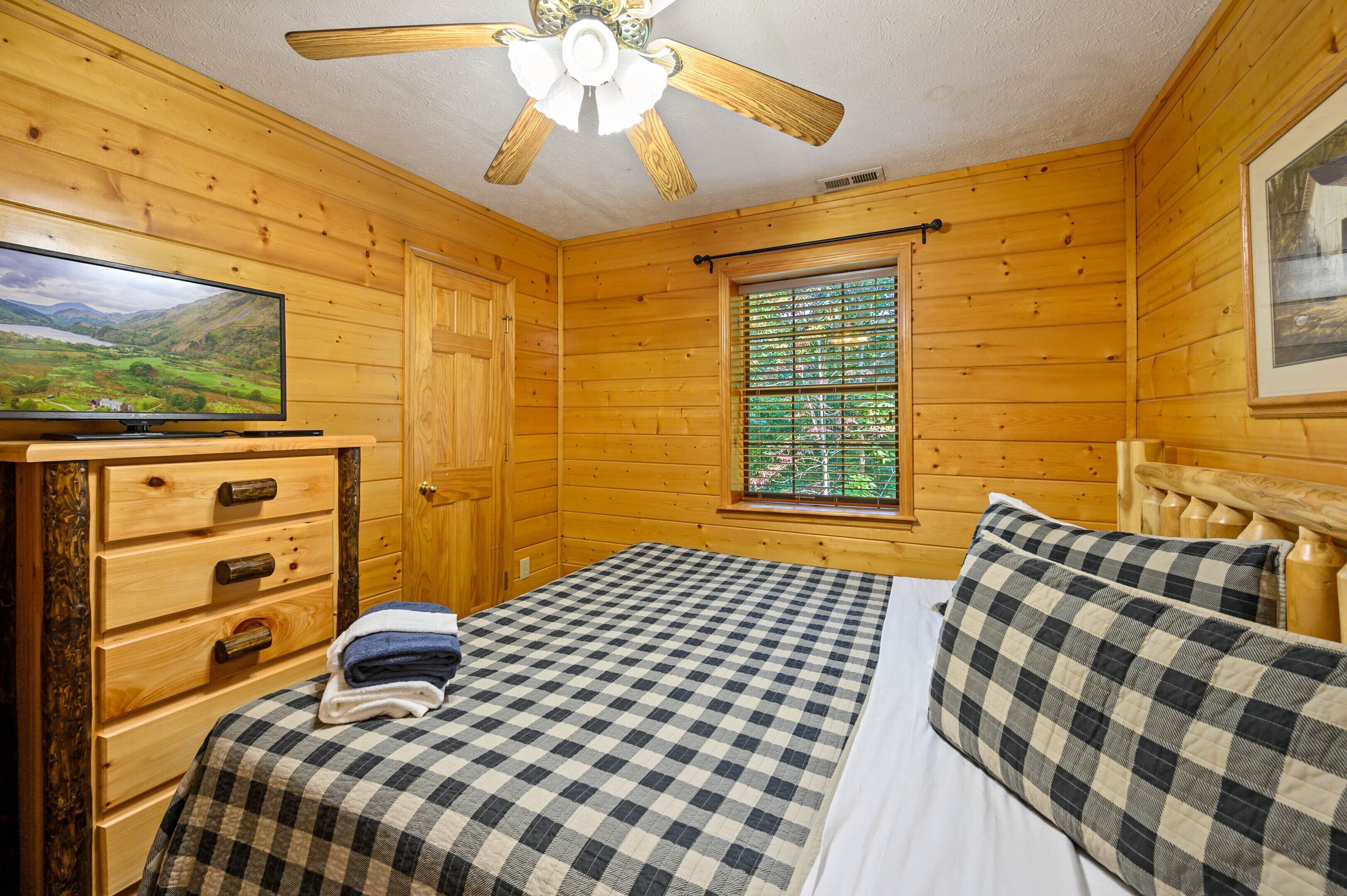 Une chambre dans un chalet en bois, comprenant un lit, un téléviseur, une commode et une fenêtre avec des stores.