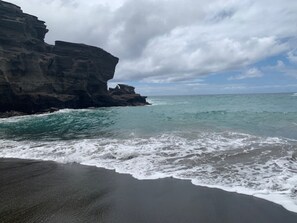 Una playa de arena oscura y un acantilado rocoso.