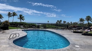 A swimming pool with a curved edge, surrounded by lounge chairs and palm trees, with a clear sky above. - #41 Turtle Hut at Punalu`u Black Sand Beach * Most (Pahala)