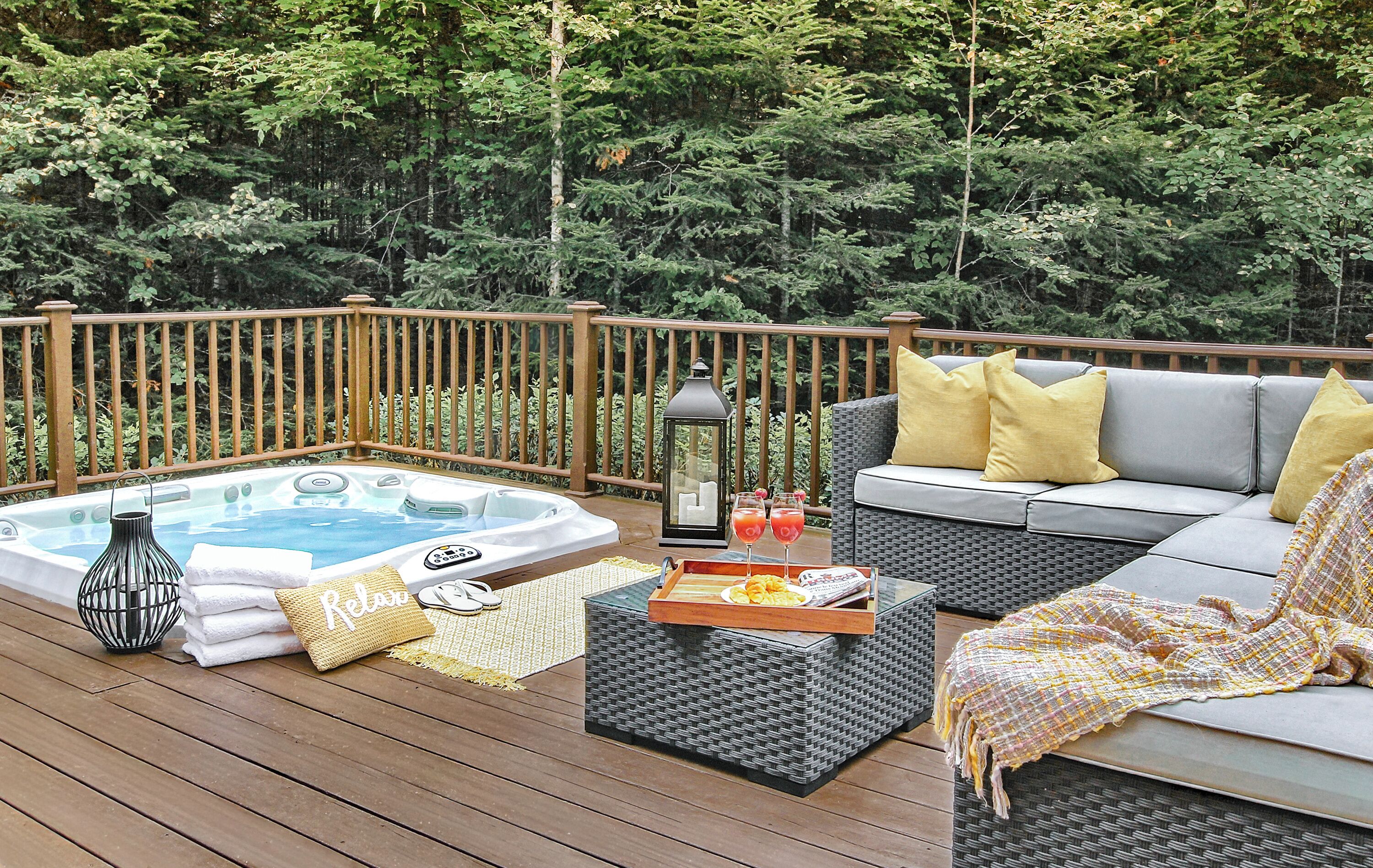 A deck with a hot tub, seating area, and a tray with drinks.