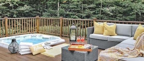 A deck with a hot tub, seating area, and a tray with drinks.