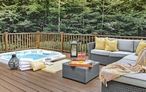 A deck with a hot tub, seating area, and a tray with drinks.