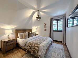Ein Schlafzimmer mit einem hölzernen Kopfteil, einem großen Bett mit gestreifter Bettwäsche, einem Nachttisch mit Lampe und einem Fenster mit Vorhängen.