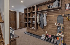 A storage area with shelves for helmets and jackets, a snowboard rack, and a shoe rack with various footwear.