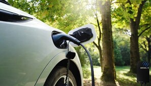 Ein weißes Auto, das an einer Ladestation für Elektrofahrzeuge in bewaldeter Landschaft angeschlossen ist.