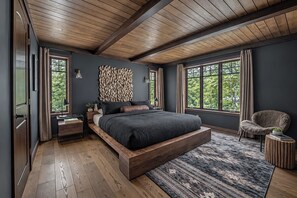 Ein Schlafzimmer mit einem großen Bett, Holzbalken an der Decke und großen Fenstern mit Vorhängen.