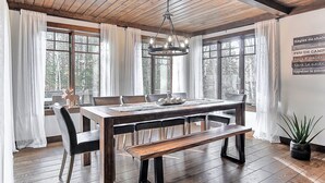 Un espace repas comprenant une table en bois, des chaises, un banc, un lustre et une plante en pot.