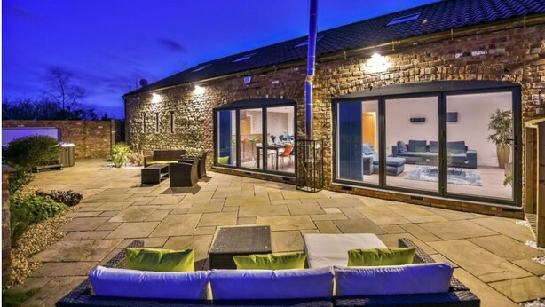 A brick building with a patio area featuring outdoor seating and a glass door leading to an interior space. - Lincoln 4-beds, Sleeps 13, Hot Tub & Pet Friendly (Lincoln)
