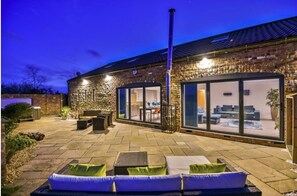 A brick building with a patio area featuring outdoor seating and a glass door leading to an interior space. - Lincoln 4-beds, Sleeps 13, Hot Tub & Pet Friendly (Lincoln)