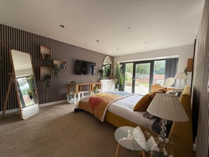 A modern bedroom with a large bed, a television, and a balcony with a view. - Lincoln 4-beds, Sleeps 13, Hot Tub & Pet Friendly (Lincoln)