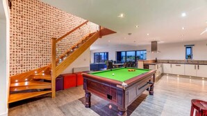 A modern home interior with a pool table, a staircase with a patterned wall, and a kitchen area. - Lincoln 4-beds, Sleeps 13, Hot Tub & Pet Friendly (Lincoln)