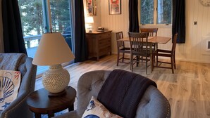 Een gezellige woonkamer met een bank, een tafel en een lamp. Er is een raam met gordijnen, een klok aan de muur en een ingelijste foto.