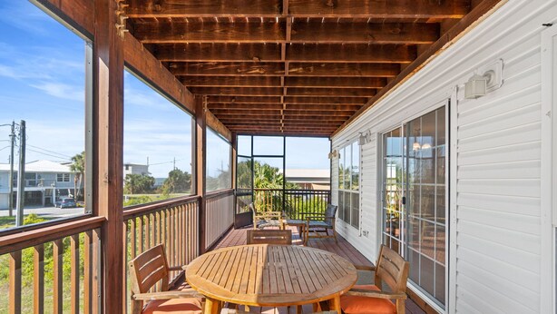Une terrasse en bois avec une table ronde et des chaises, une rambarde et une vue sur la rue.