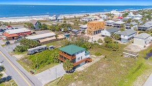Vue aérienne d’une zone résidentielle côtière, avec des maisons, une plage et un ciel dégagé.