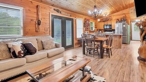 A wooden cabin interior with a sofa, dining table, chairs, kitchen area, and a chandelier. - Holy Smokes - 2 bdrms/2 bath, fire pit, pet friendly with yard (Townsend)