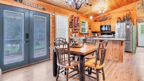 A wooden cabin interior with a dining table, chairs, a chandelier, and a kitchen area. - Holy Smokes - 2 bdrms/2 bath, fire pit, pet friendly with yard (Townsend)