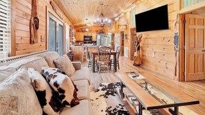 A cozy cabin interior with a wooden interior, a dining area, and a TV mounted on the wall. - Holy Smokes - 2 bdrms/2 bath, fire pit, pet friendly with yard (Townsend)