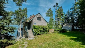 Ett litet hus i ett våningsplan med en veranda och utsikt över en sjö.