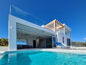 A modern two-story house with a glass facade, a swimming pool, and a wooden pergola.