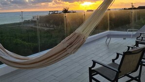 A hammock on a balcony overlooking a sunset, with chairs and a view of the sea. - VILLA CASCADA- Lux private gated villa with elevator, Private Gated Luxury Oceanview Villa with Elev (Isla Mujeres)