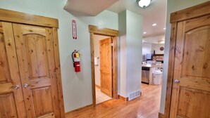 Un corridoio con porte in legno, un estintore e una zona cucina sullo sfondo.