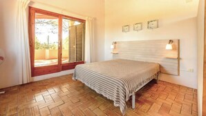 Un dormitorio con cama, piso de madera, ventana con contraventanas e iluminación en la pared.