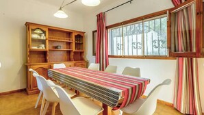 Un comedor con una mesa de madera y sillas blancas, un armario de madera con estantes, y una ventana con cortinas.