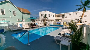 A pool area with lounge chairs and umbrellas, surrounded by buildings with a white and teal color scheme.