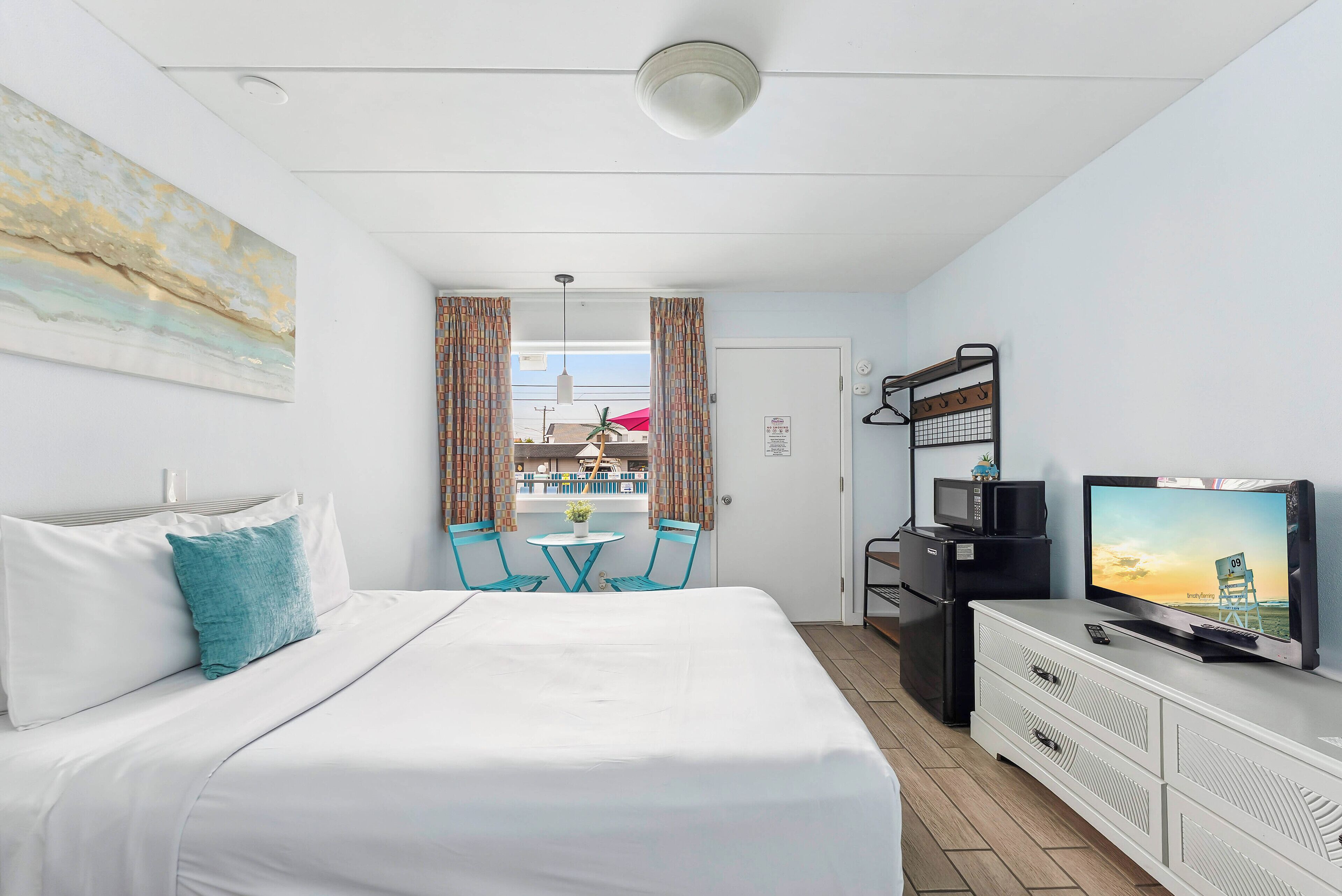 A hotel room with a bed, a TV, a desk, and a view of the outside.