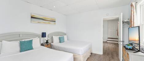 A hotel room with two beds, a nightstand, a lamp, a painting, and a view of the sunset through a window.