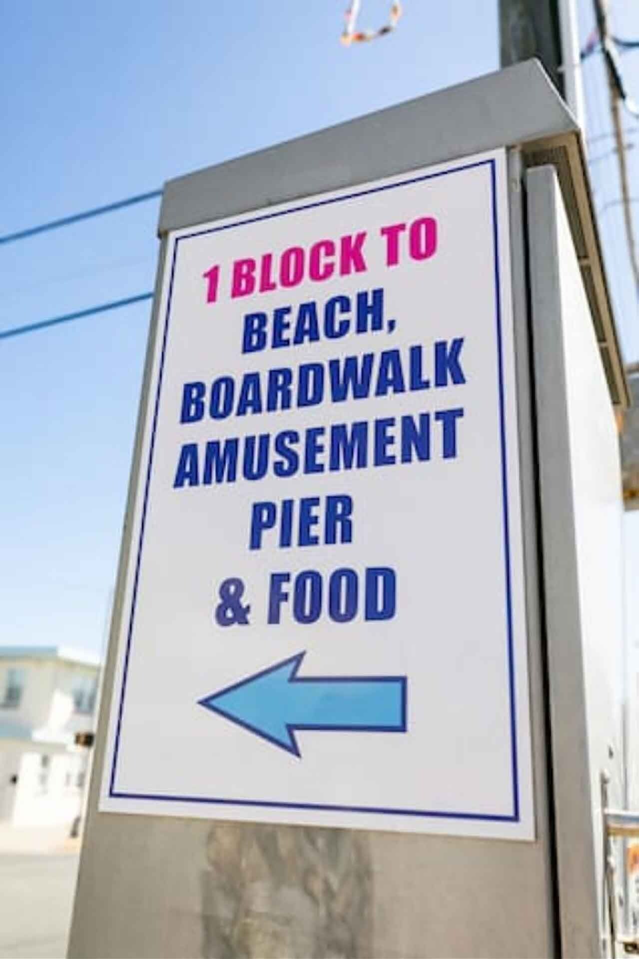 Wegwijzer die aangeeft: '1 blok naar strand, pier, attracties en eten', met een pijl naar links.
