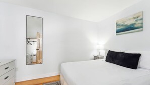 Een slaapkamer met een bed, een dressoir, een spiegel, een nachtkastje en een schilderij aan de muur.