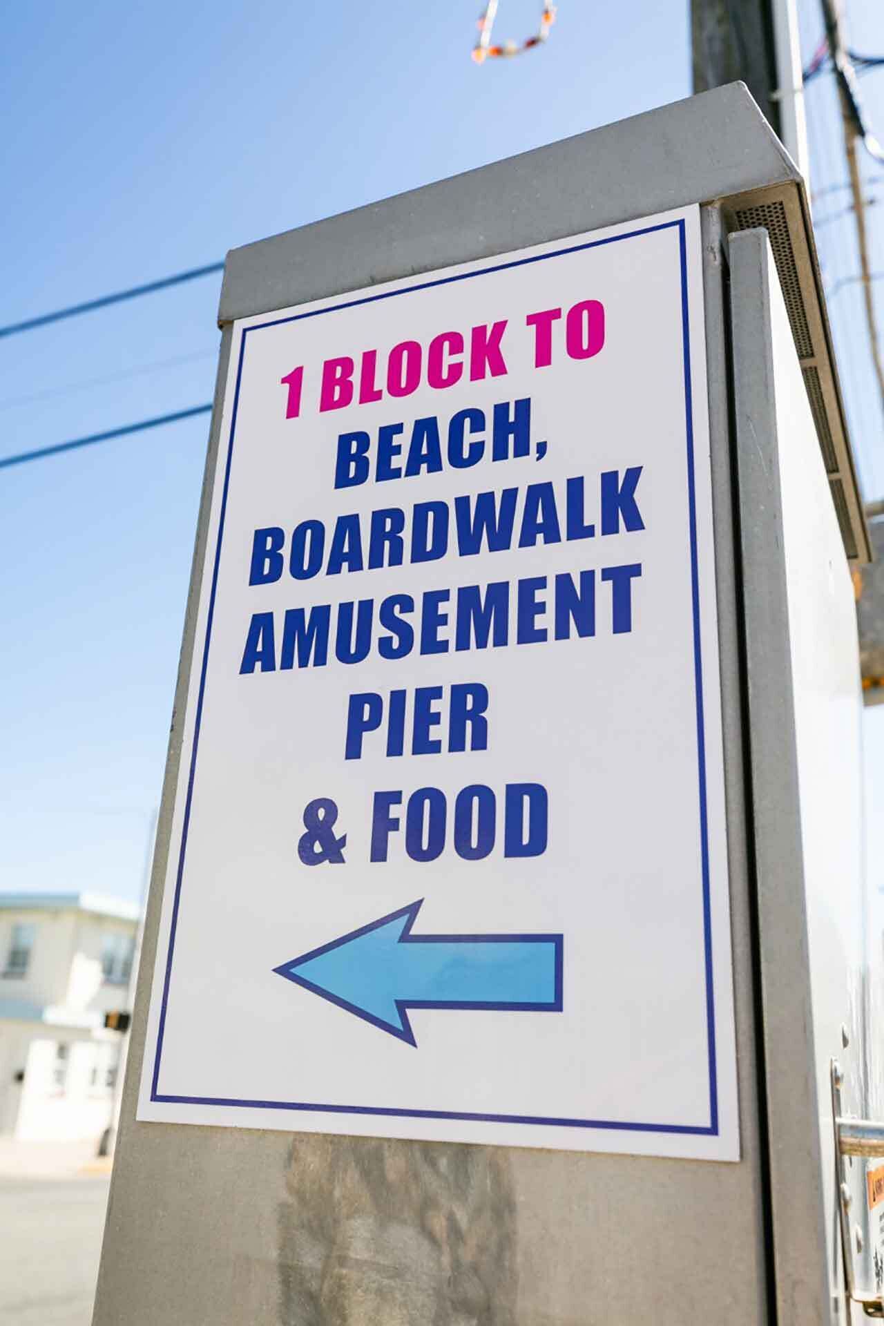 A directional sign indicating attractions 1 block away, including beach, boardwalk, amusement pier, and food.
