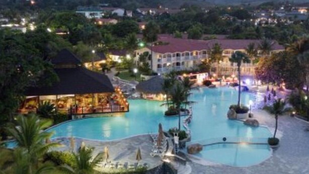 A resort with a large swimming pool, multiple buildings, and a mountainous backdrop. - Junior Suites – The Tropical (Puerto Vallarta)