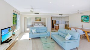 A modern living room with a sofa, TV, and a dining area with chairs and a table.