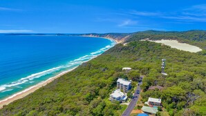 An aerial view of a coastal area with a beach, dense forest, and residential buildings.