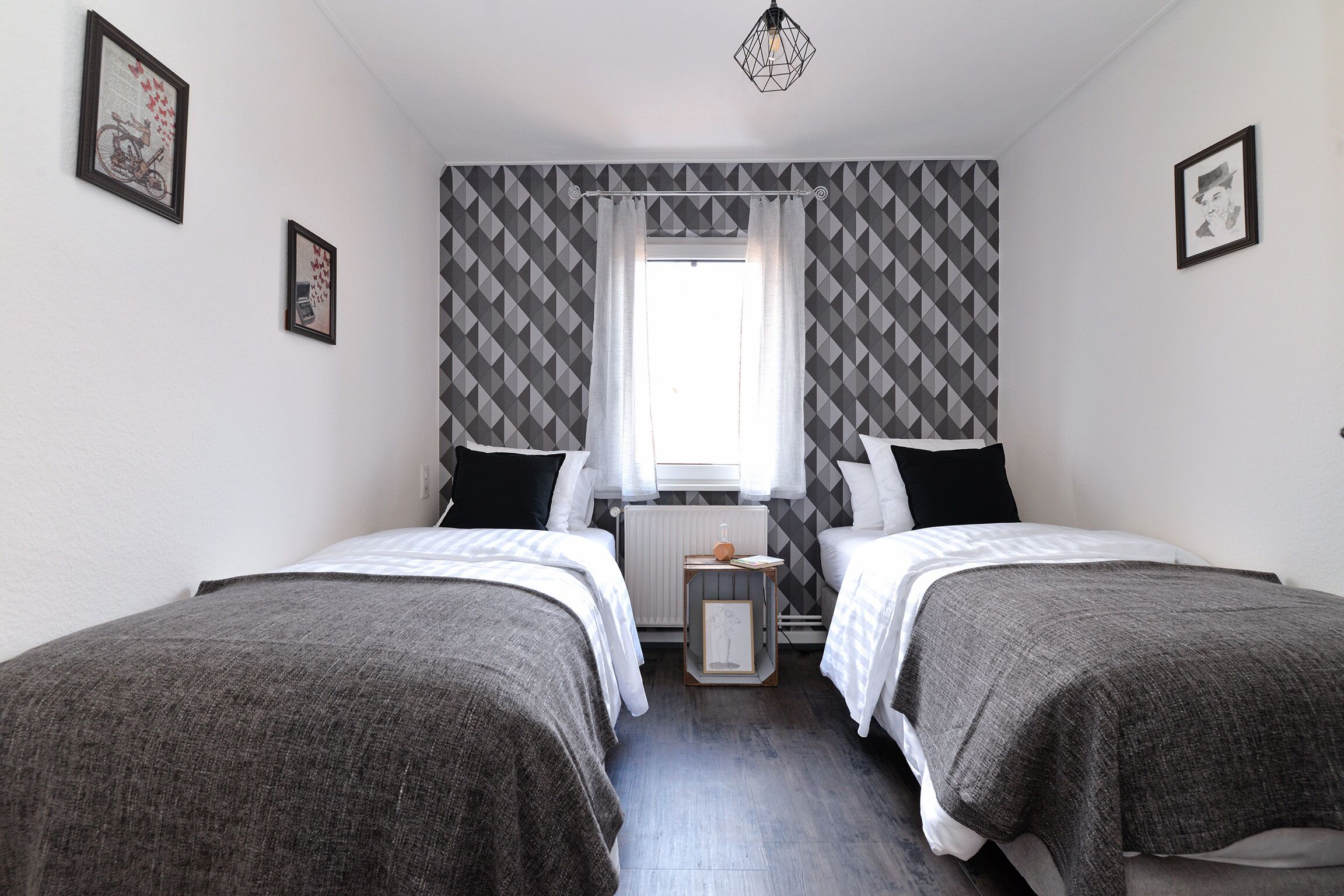A bedroom with two beds, a small bedside table, and a window with curtains.