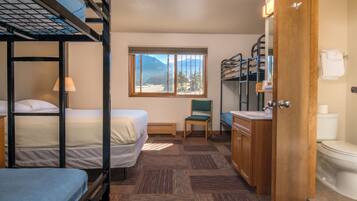 A compact hotel room with bunk beds, a small seating area, a window with a mountain view, and a wooden door.