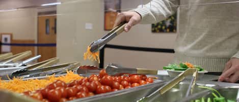A buffet with various food items including shredded cheese, cherry tomatoes, and greens.
