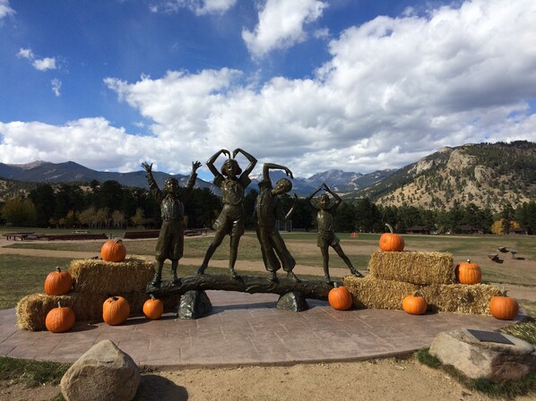 A sculpture of children on a log with hay bales and pumpkins in a park with mountains in the background.