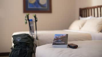 Una habitación de hotel con una cama, un libro titulado "Hiking the Rocky Mountains National Park", una mochila y un par de esquíes apoyados contra la pared.