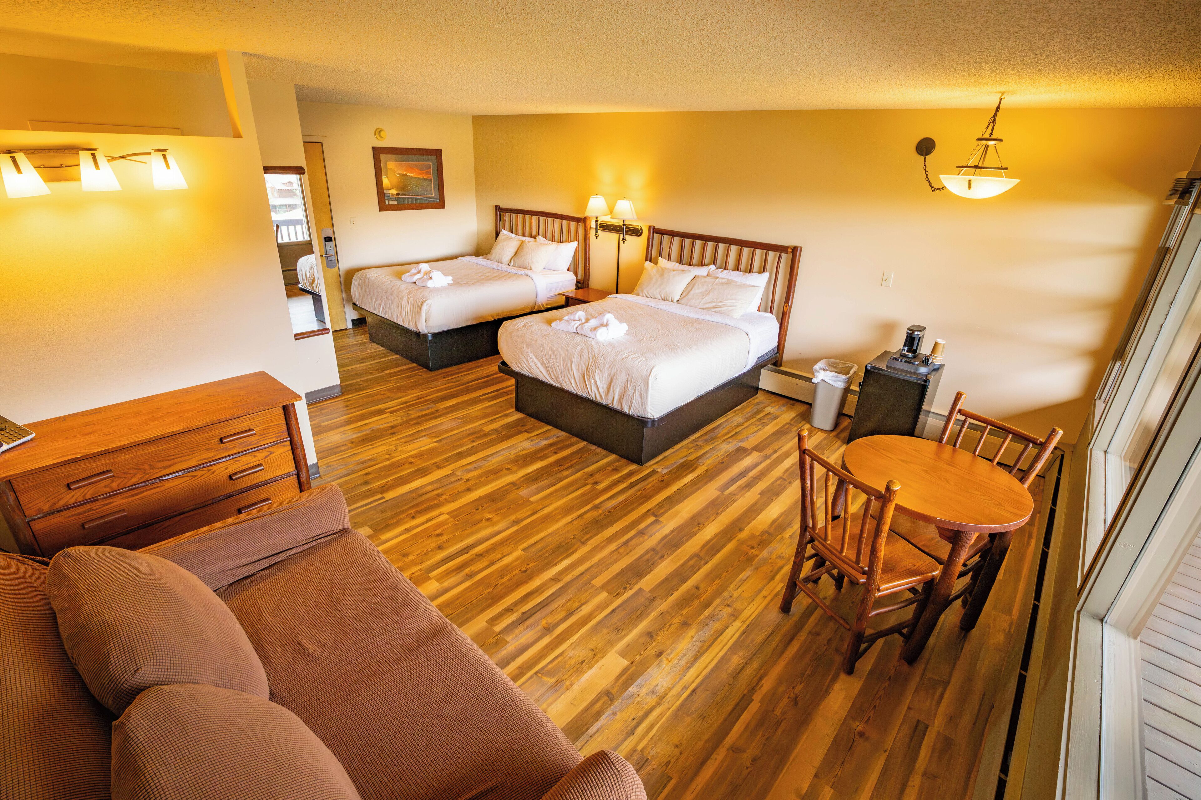 A hotel room with two beds, a wooden floor, a dining table with chairs, and a sofa.