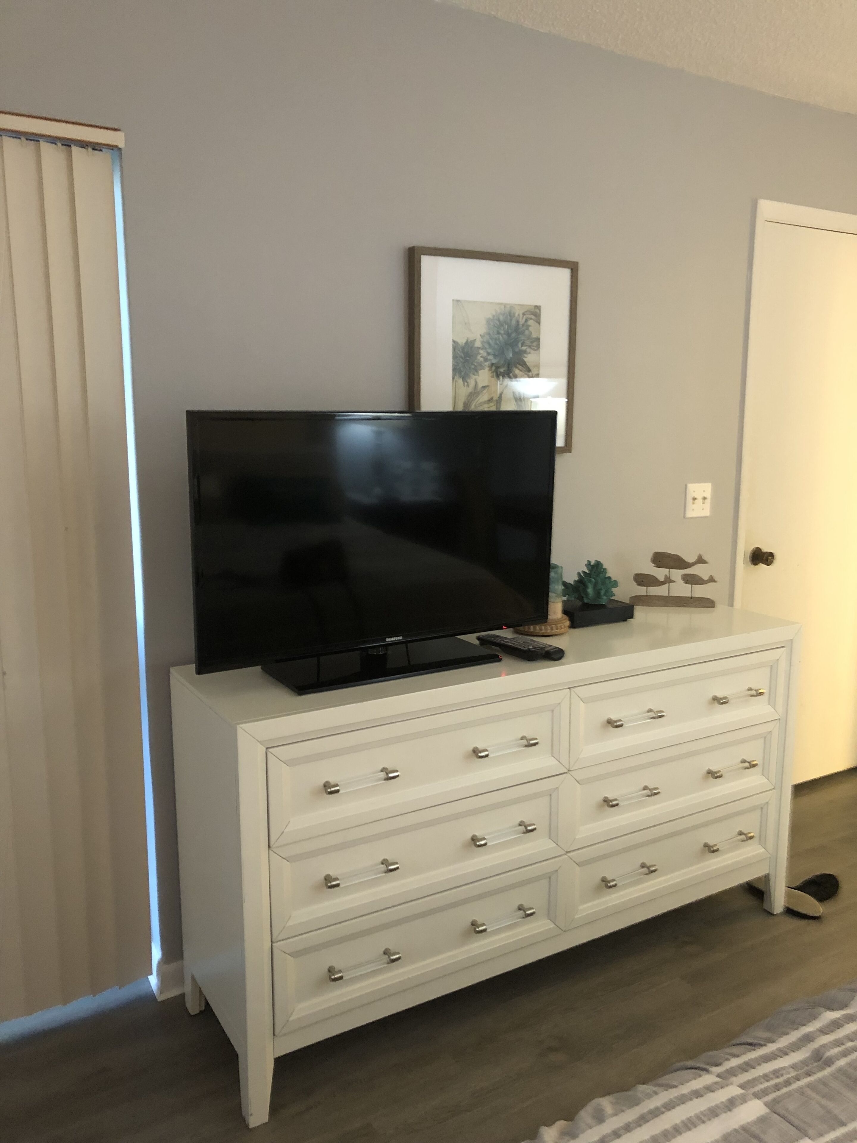 A white entertainment center with a flat-screen TV, a framed artwork, and a small plant.