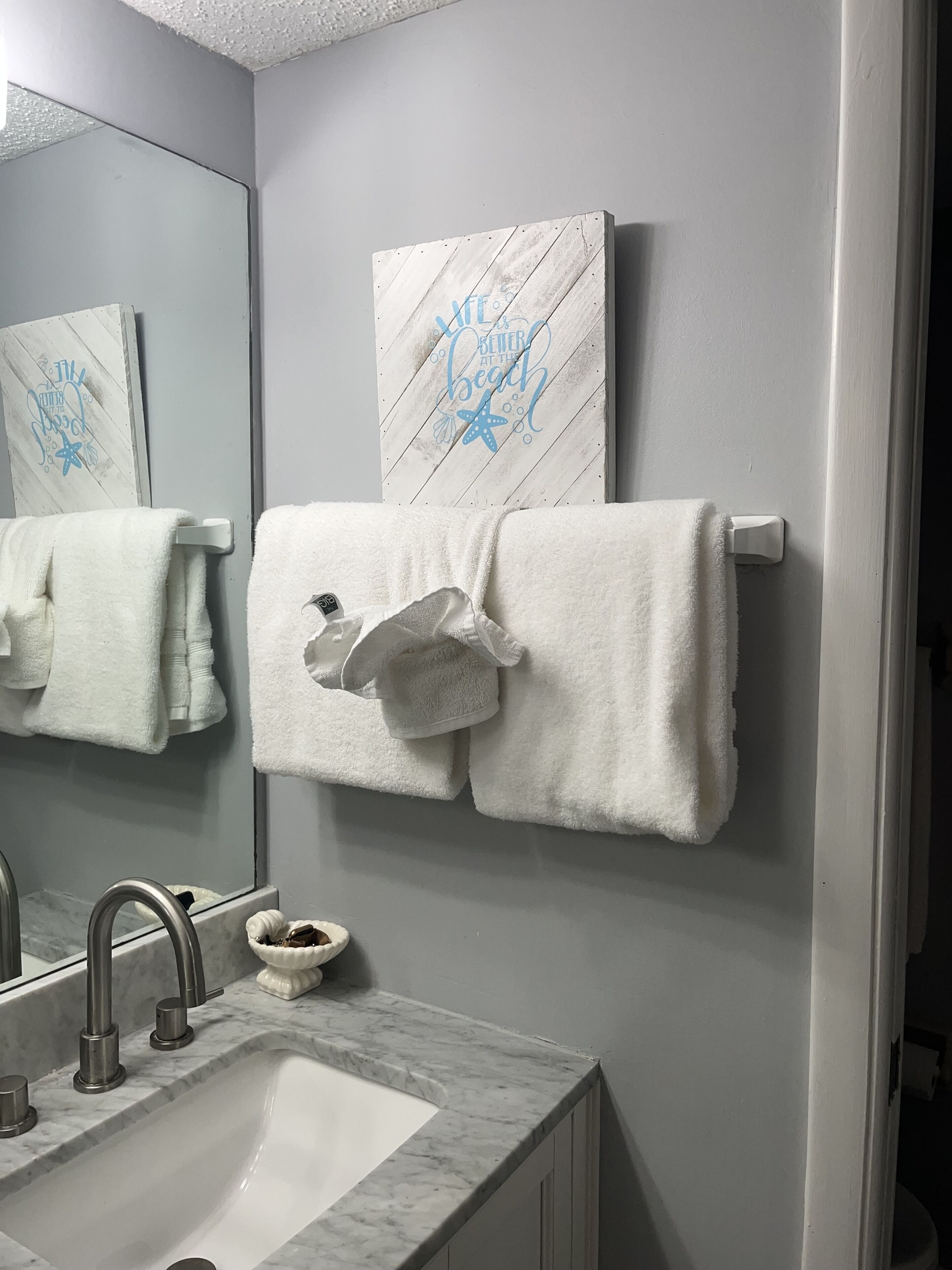 Un baño con lavamanos de mármol, un perchero con dos toallas, un adorno de pared y un espejo.