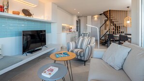 Ett modernt vardagsrum med tv, soffa och soffbord. Det finns också en köksdel med ett matbord och stolar.